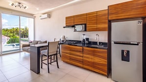 A modern kitchen with wooden cabinets, a stainless steel refrigerator, and a large window offering a view of palm trees.