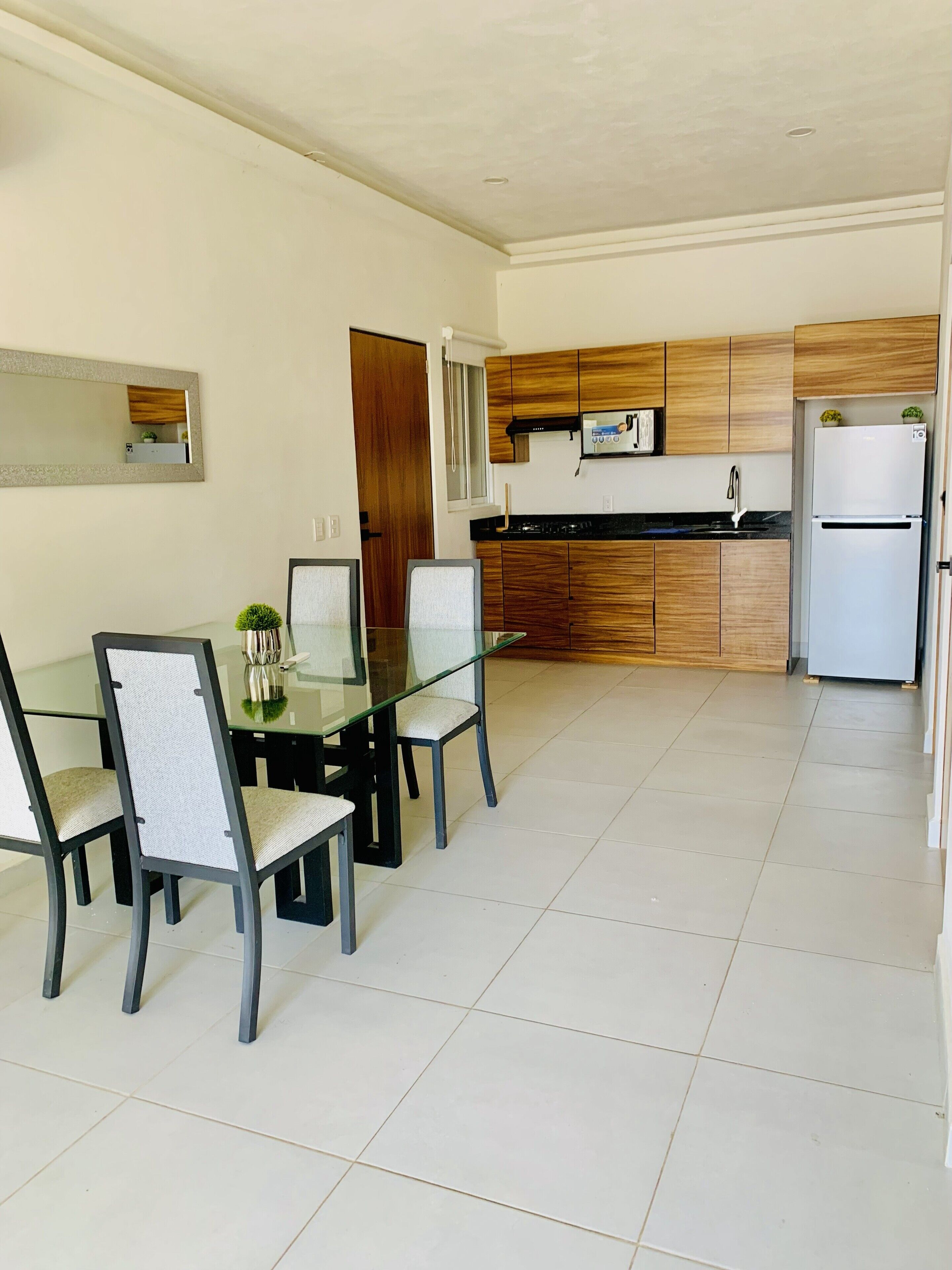 A modern kitchen with wooden cabinets, a white refrigerator, and a dining area with a glass table and chairs.