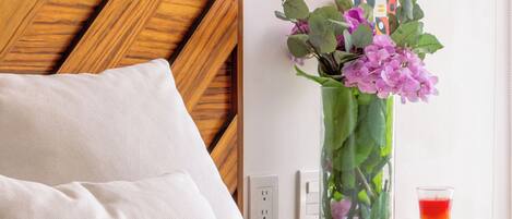 A neatly made bed with white bedding, a wooden headboard, a vase with flowers, and a small table with a red candle.