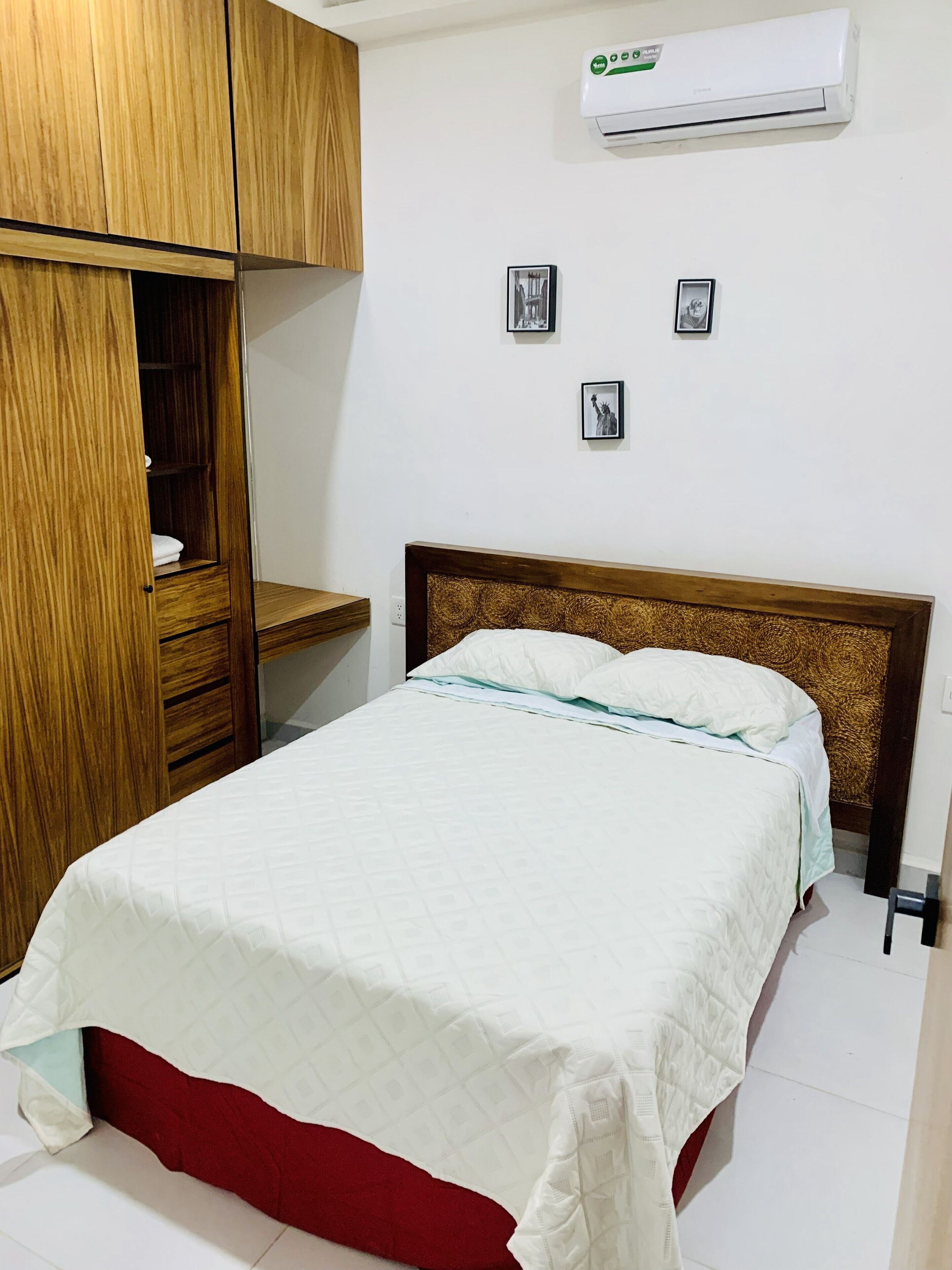 A bedroom with a bed, a wooden wardrobe, and an air conditioning unit on the wall.