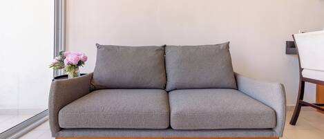 Un sofá gris con patas de madera en una habitación moderna con pared blanca y ventana.