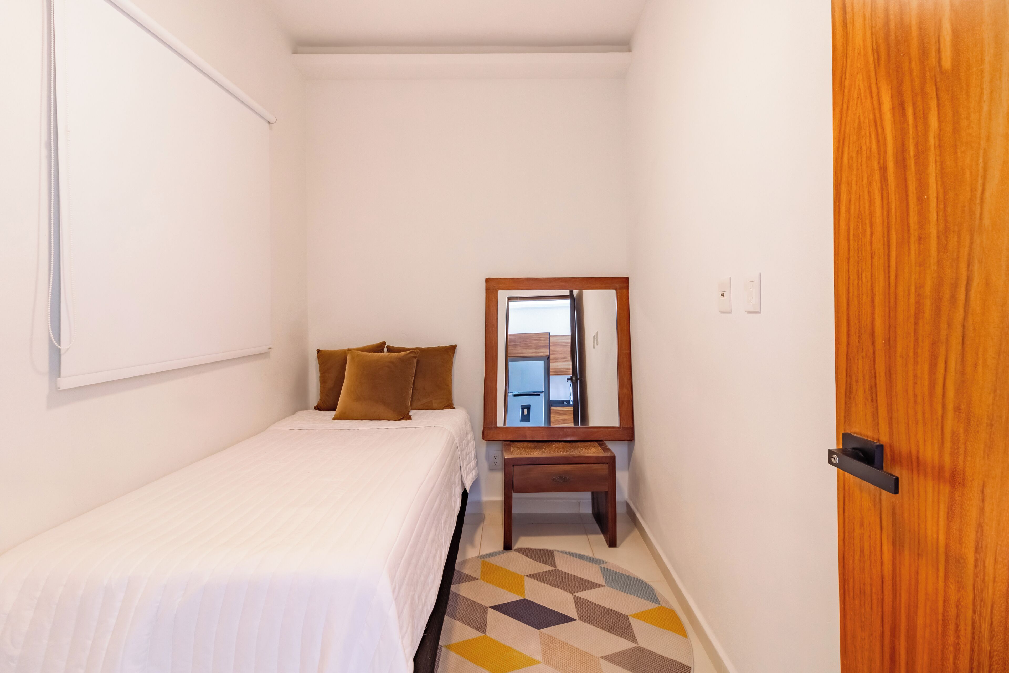 Une chambre à coucher avec un lit, une table de chevet en bois, un miroir et une porte.