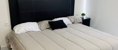 Una cama bien hecha con un cabecero negro, una colcha color beige y dos almohadas.