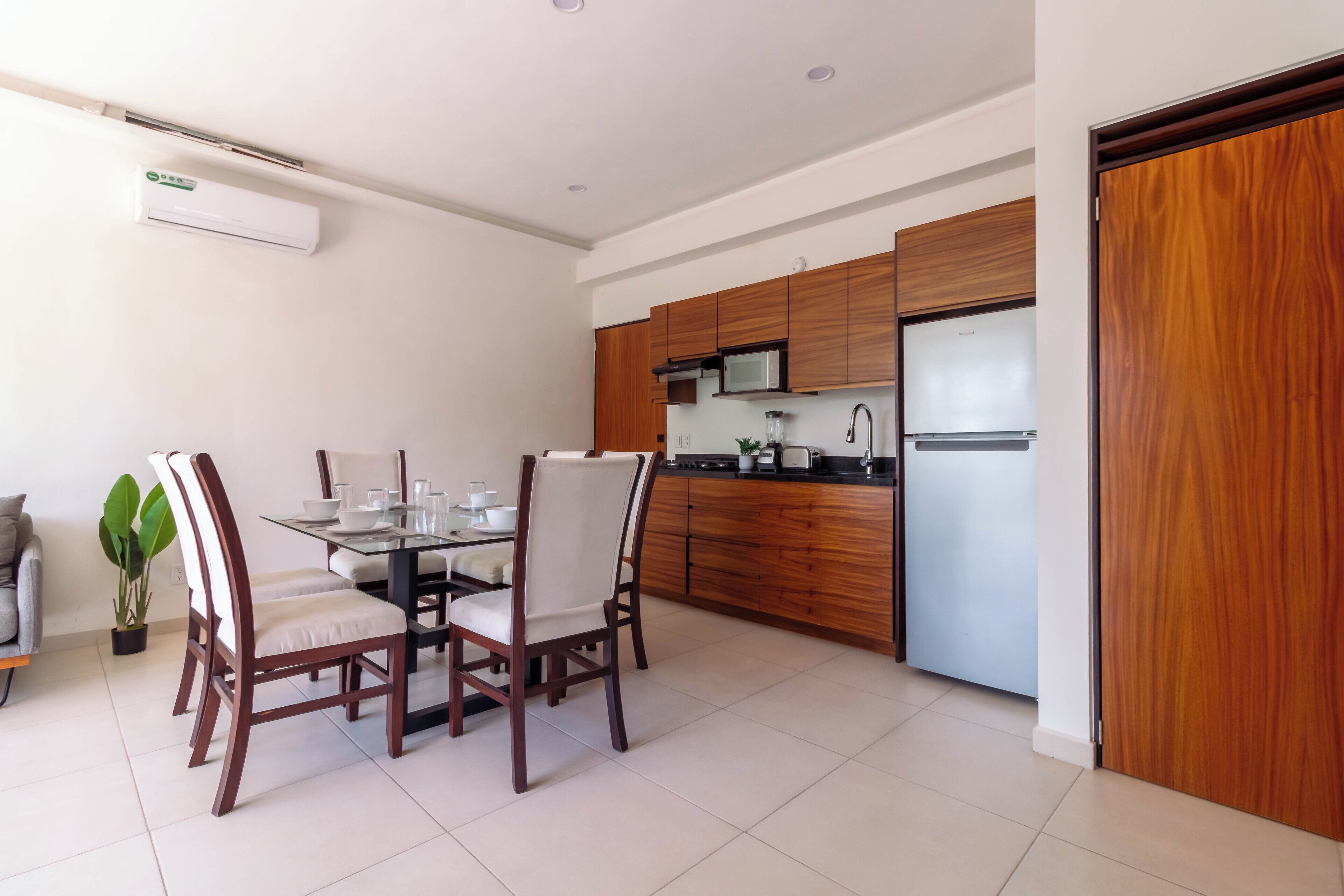 A modern kitchen with wooden cabinets, a stainless steel refrigerator, and a dining area with a glass table and wooden chairs.