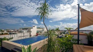 A rooftop pool with a view of the cityscape, surrounded by palm trees and a clear sky. - Steps from 5th Ave, 2 Bedroom Luxury Condo, 2 Baths, 4 min to Beach,Rooftop Pool (Playa del Carmen)