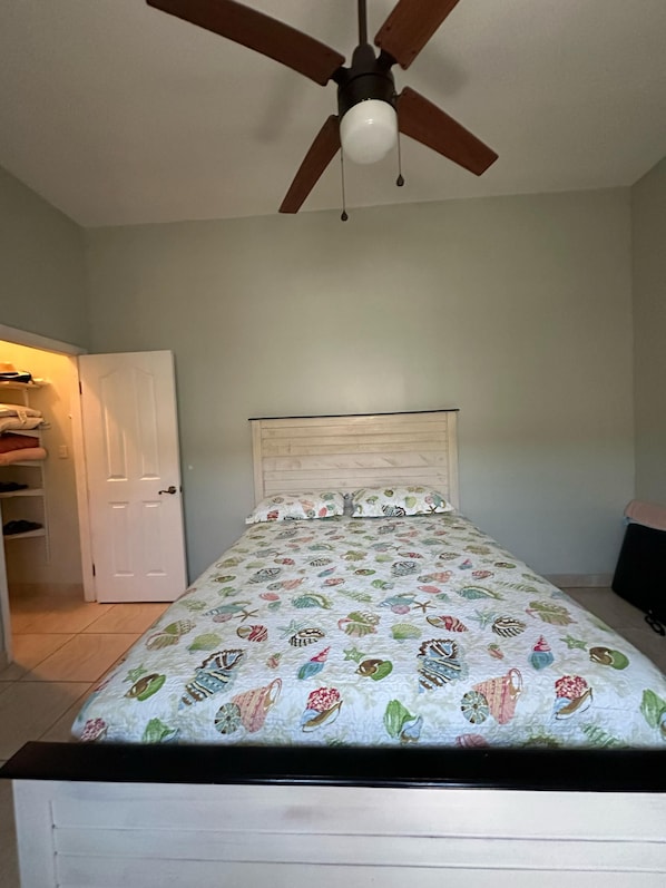 A bedroom with a bed, a ceiling fan, and a door.