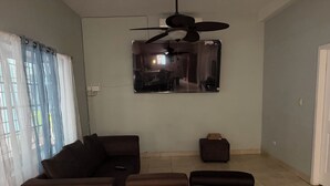 Un soggiorno con divano, poggiapiedi, ventola a soffitto e televisore montato a parete.