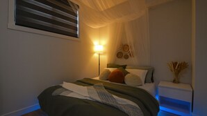 A bedroom with a bed, bedside table, lamp, and decorative wall items. - CASA BOHO I Cozy Boho Retreat in NW Calgary (Calgary)