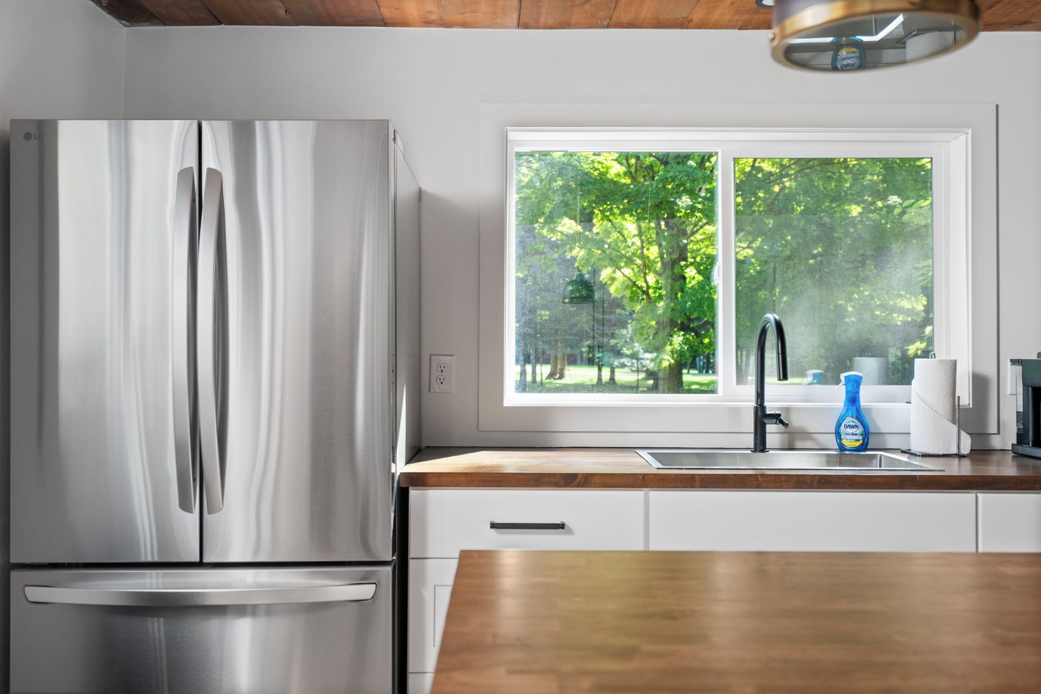 Una cocina moderna con un refrigerador de acero inoxidable, una encimera de madera y una ventana con vista a árboles.