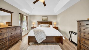A bedroom with a large bed, wooden dresser, and a ceiling fan. - Modern Getaway-Private Tub & Game Room (Ocala)