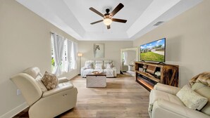A spacious living room with a ceiling fan, a large flat-screen TV, and a wooden coffee table. - Modern Getaway-Private Tub & Game Room (Ocala)