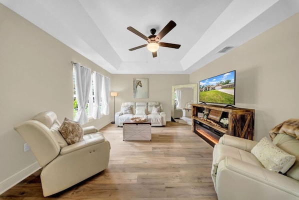 Un salon spacieux doté d’un ventilateur de plafond, d’un grand téléviseur à  écran plat et d’une table basse en bois.