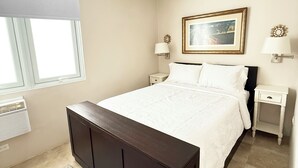 A bedroom with a large bed, a ceiling fan, bedside lamps, a framed picture on the wall, and a window with blinds.