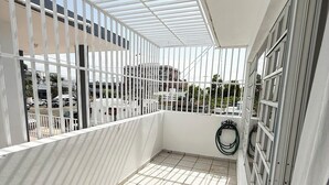 A balcony with a tiled floor, white railings, and a view of buildings and parked cars.