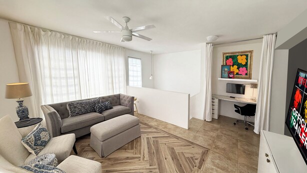 A modern living room with a sofa, ottoman, and a desk area with a computer.