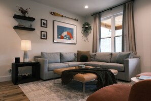 A modern living room with a grey sofa, a coffee table, a side table with a lamp, and a framed artwork on the wall.
