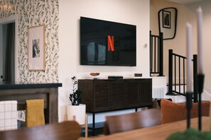 Un salon moderne doté d’un grand téléviseur à écran plat fixé au mur, d’une console en bois foncé et d’un escalier avec des rampes noires.