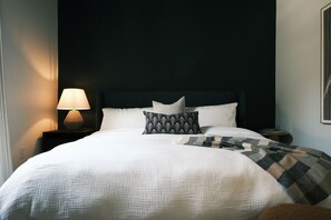 A neatly made bed with a patterned pillow, a bedside lamp, and a dark headboard.