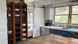 Eine rustikale Küche mit sichtbaren Holzbalken, einem großen Holztisch und einer eingebauten Regalausstattung mit Geschirr.
