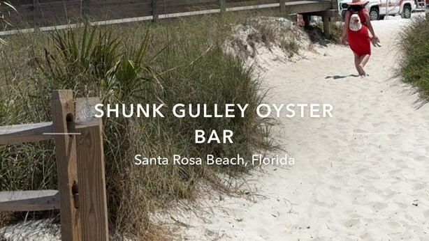 Eine Strandansicht mit einem hölzernen Steg, der zum Meer führt, einem Rettungsschwimmturm und einem Fahrzeug mit einem roten Sonnenschirm. Text gibt an, dass sich der Ort Shunk Gulley Oyster Bar, Santa Rosa Beach, Florida, befindet.