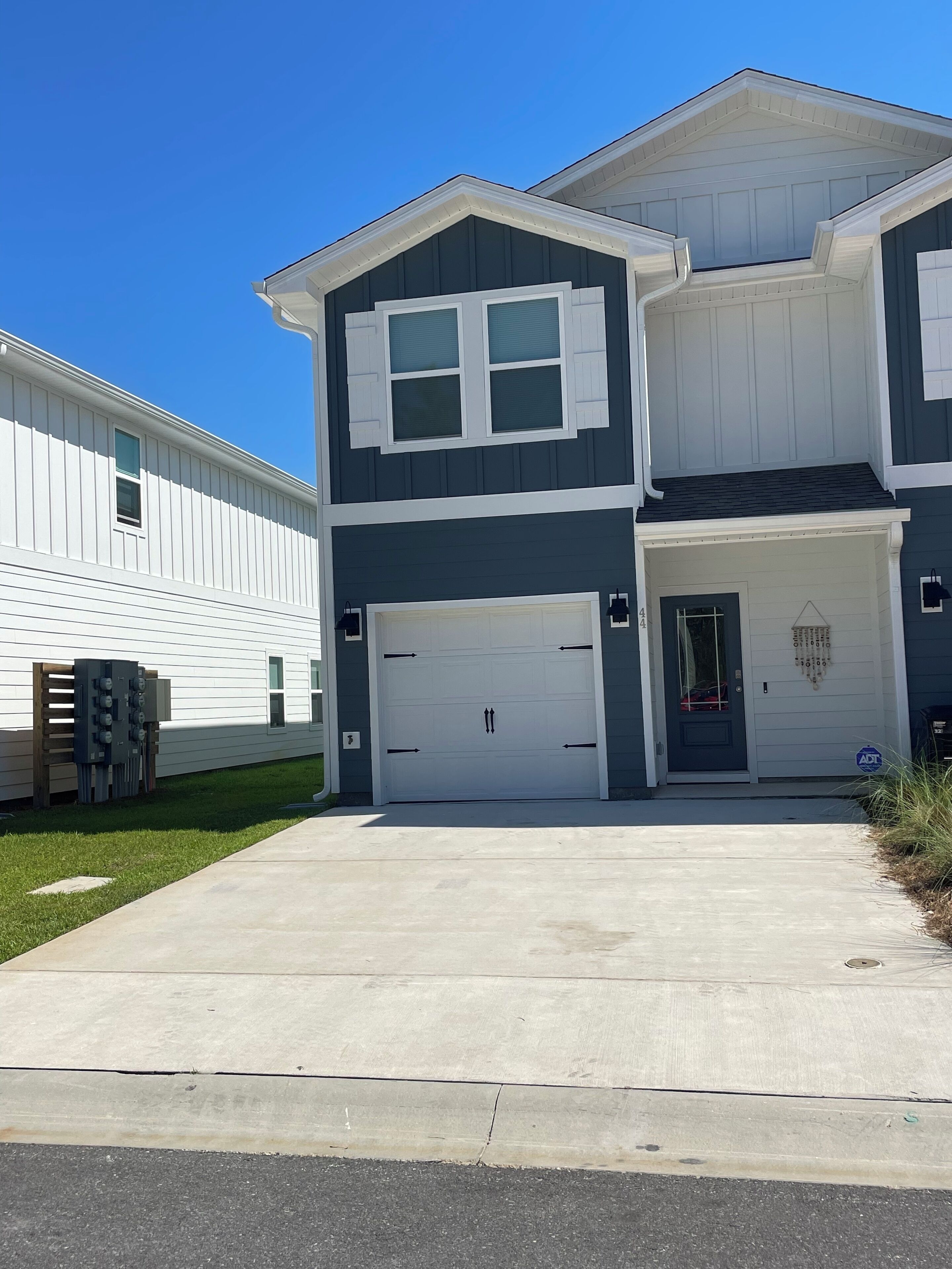 A two-story residential building with a garage, a small porch, and a clear blue sky.