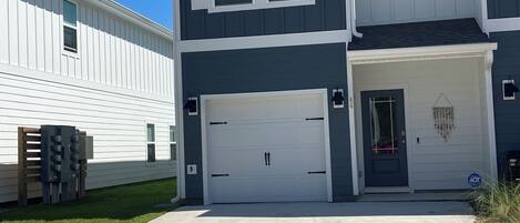 A two-story residential building with a garage, a small porch, and a clear blue sky.