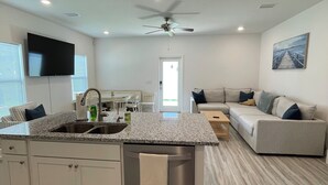 Eine moderne Küche mit Kochinsel, ein Essbereich mit Tisch und Stühlen, ein Wohnzimmer mit Sofa und Deckenventilator.