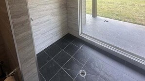 Ein modernes Badezimmer mit Dusche, Toilette und einem großen Fenster mit Blick ins Freie.