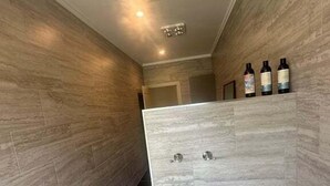 Ein Flur mit modernem Design, gekennzeichnet durch eine helle Wand und dunkle Bodenfliesen. Am Ende des Flurs befinden sich drei Flaschen auf einem Regal.