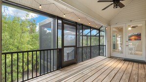 A covered porch with a wooden floor, large glass doors, and a ceiling fan. - Stunning pool home steps to beach! REDUCED! (Sanibel)