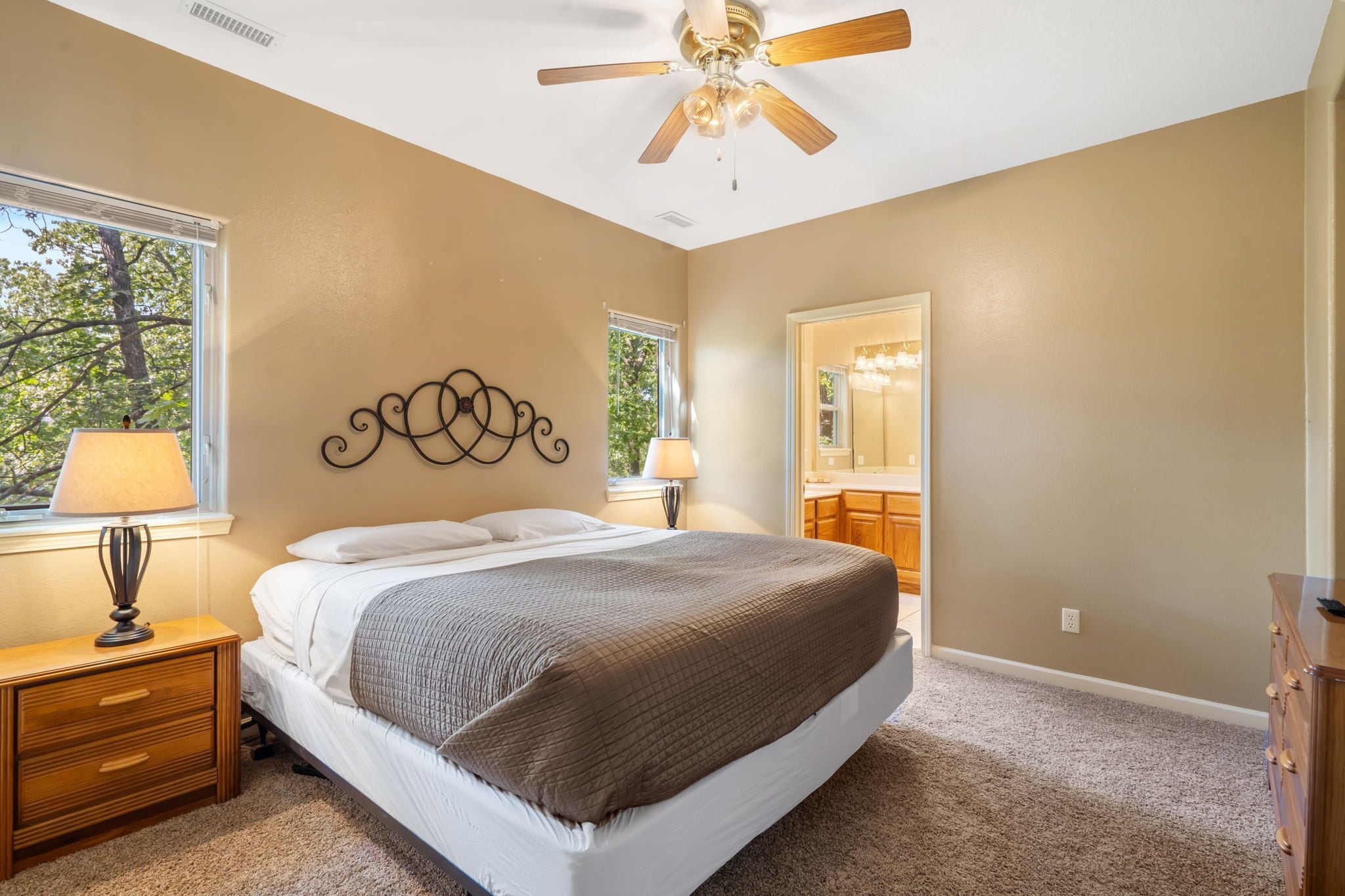 A bedroom with a bed, two bedside tables, a ceiling fan, and a window with a view of trees.