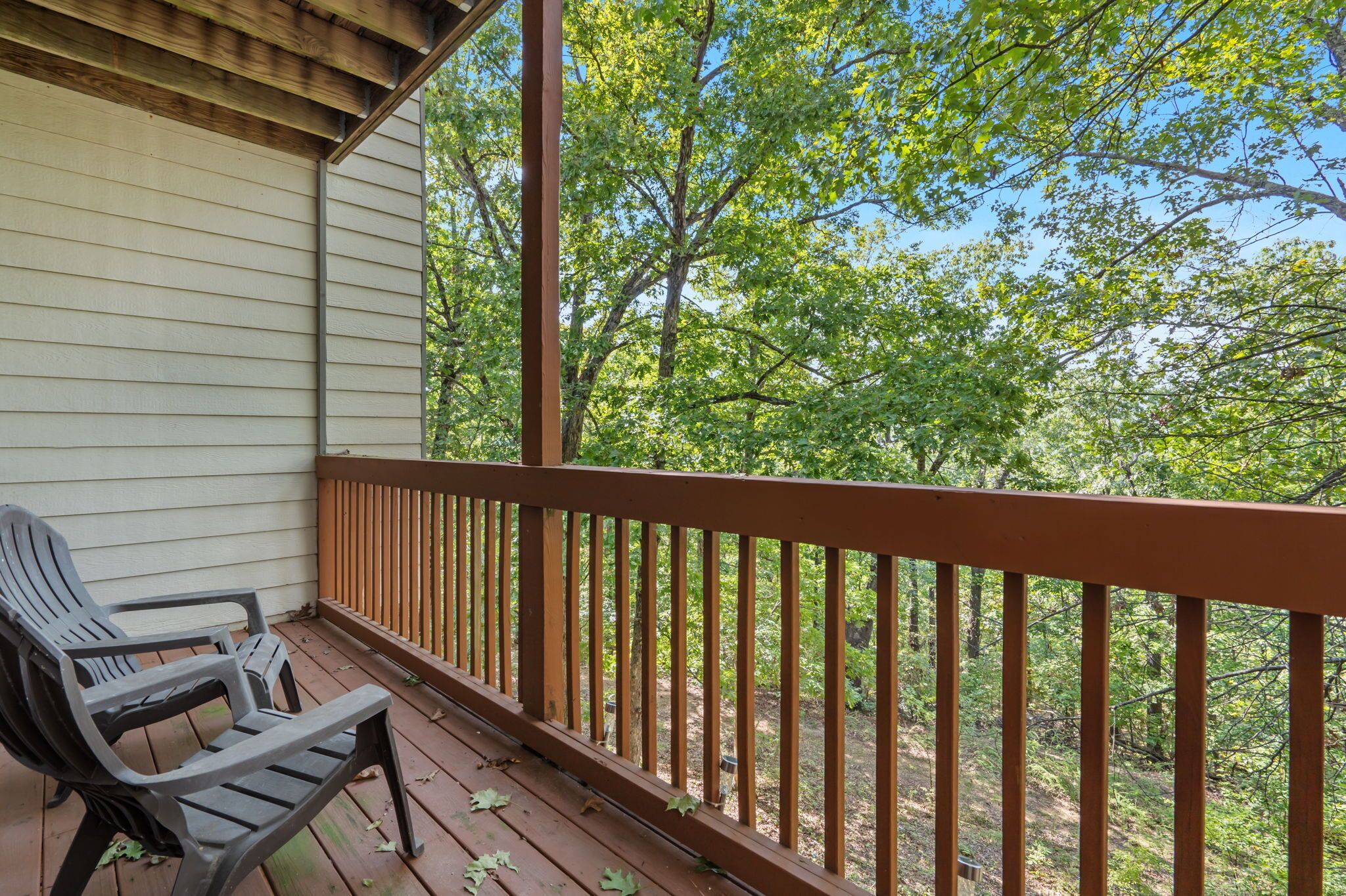 A wooden deck with a railing, a chair, and a view of trees.