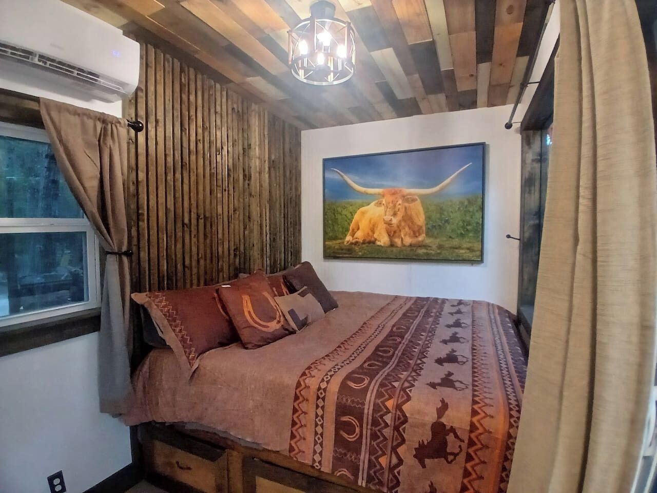 A bedroom with a bed, a window, a painting of a bull, and a wooden ceiling.