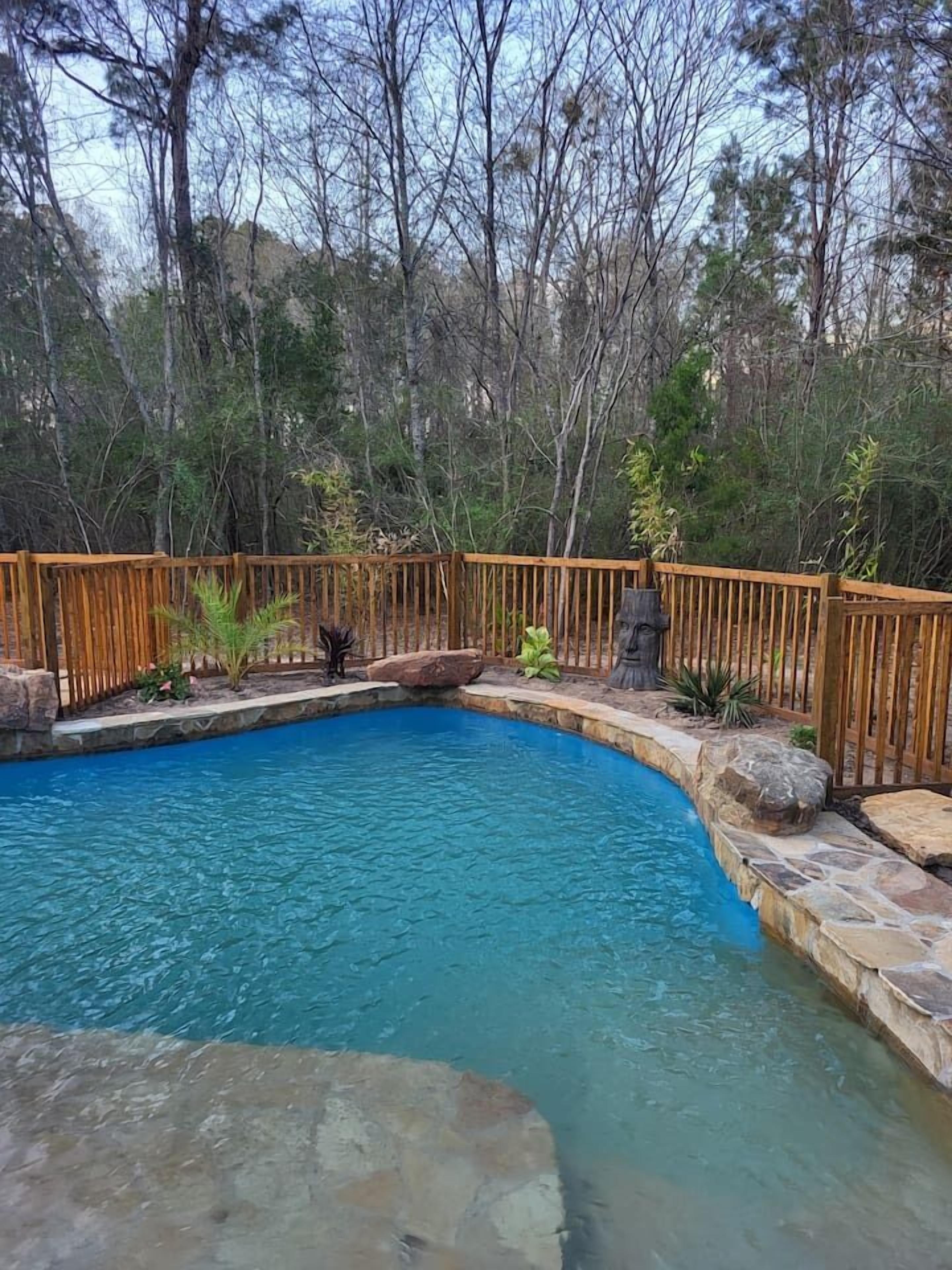 Une piscine dotée d’une terrasse en bois et bordée de pierres, entourée d’arbres.