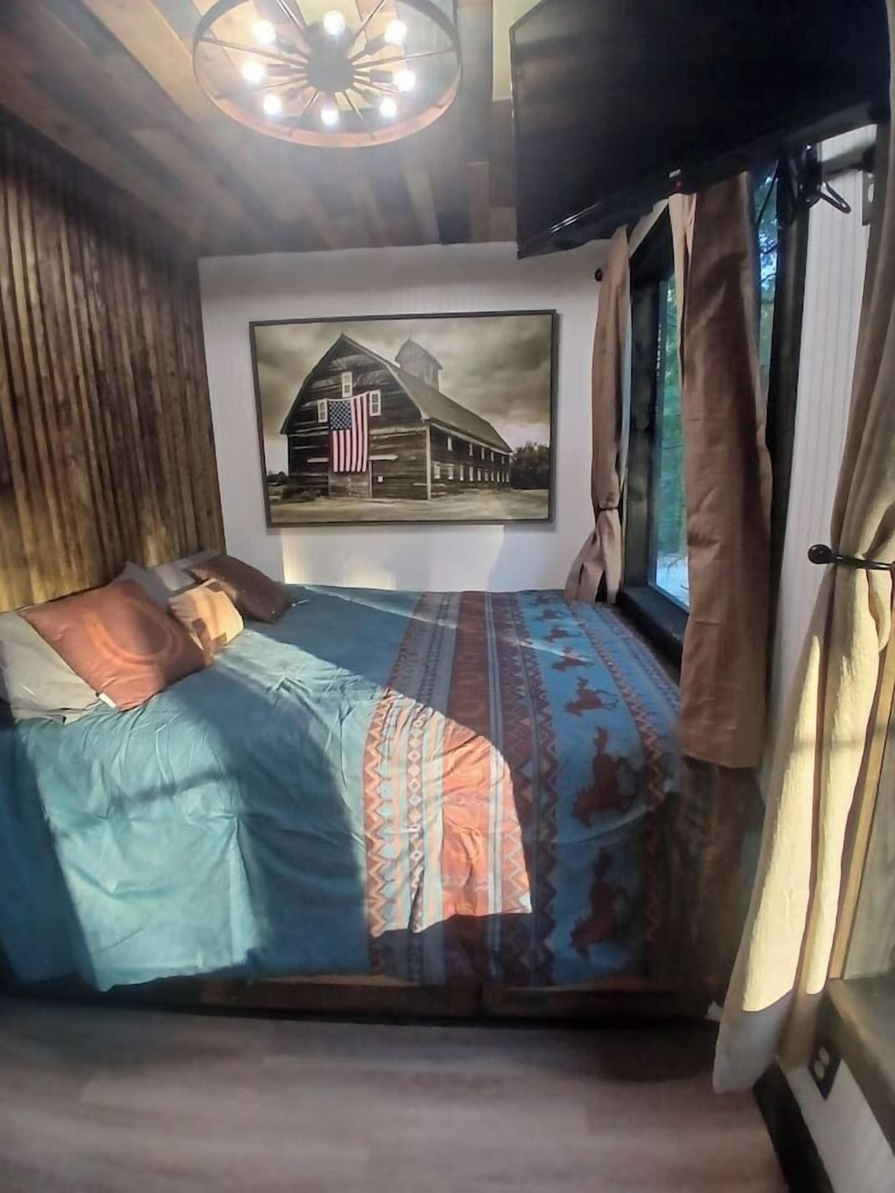 A bedroom with a bed, a mounted television, a framed picture on the wall, and curtains on the window.