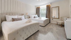 Quarto de hotel com duas camas, um candelabro, um espelho grande e uma escrivaninha.