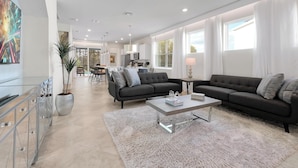Uma sala de estar moderna com sofá, mesa de centro e um espaço de jantar ao fundo.