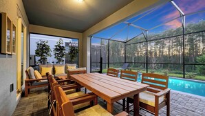 Um alpendre coberto com uma mesa e cadeiras de madeira, uma piscina e vista para uma floresta.