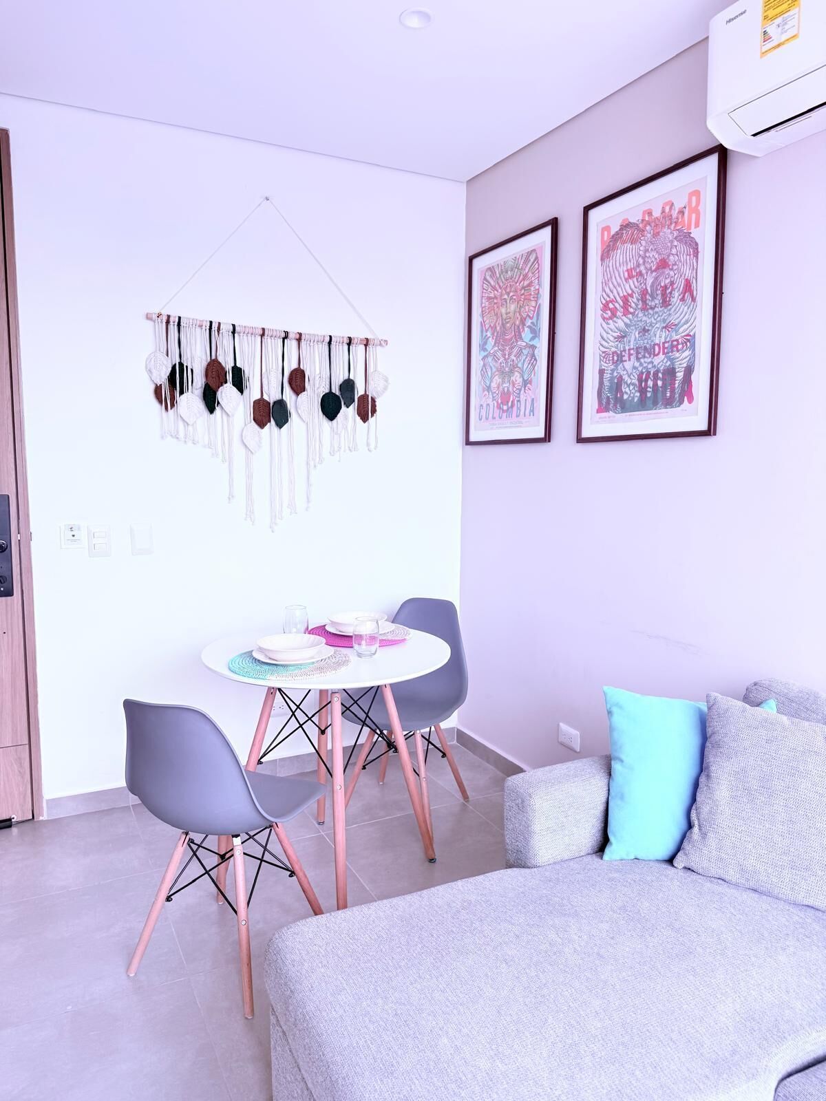 A modern living room with a grey sofa, a small round table with chairs, and two framed artworks on the wall.