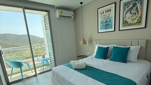 A modern hotel room with a large bed, a view of the outdoors, and a balcony with chairs. - Cozy Apartment One Block from the Ocean in Salguero Beach, Santa Marta (Gaira)