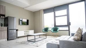 Un salon moderne avec un canapé gris, deux fauteuils verts, un téléviseur à écran plat et une grande fenêtre donnant sur un beau paysage.