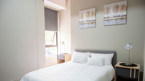Une chambre à coucher comprenant un lit, une table de chevet, une lampe et deux tableaux accrochés au mur.