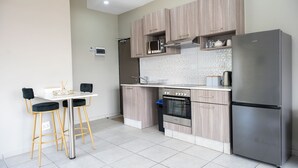 Une cuisine moderne avec des meubles en bois, un réfrigérateur en acier inoxydable, un four encastré et un petit coin repas équipé de deux tabourets de bar.