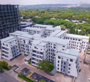 Un bâtiment moderne à plusieurs étages, à la structure quadrillée, entouré de verdure et d’autres immeubles.