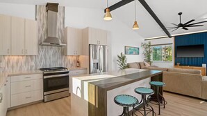 Eine moderne Küche mit Kochinsel, Barhocker und einem Essbereich mit Sofa und Fernseher.