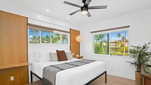 Ein modernes Schlafzimmer mit einem Bett, einem Deckenventilator und großen Fenstern mit Blick auf Palmen und Gebäude.