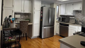 A modern kitchen with white cabinets, a stainless steel refrigerator, a microwave, and a ceiling fan. - Valerie’s Villa - free WiFi - 3 tv’s - 15 mins to beach - 30 second walk to pool (Fort Myers)