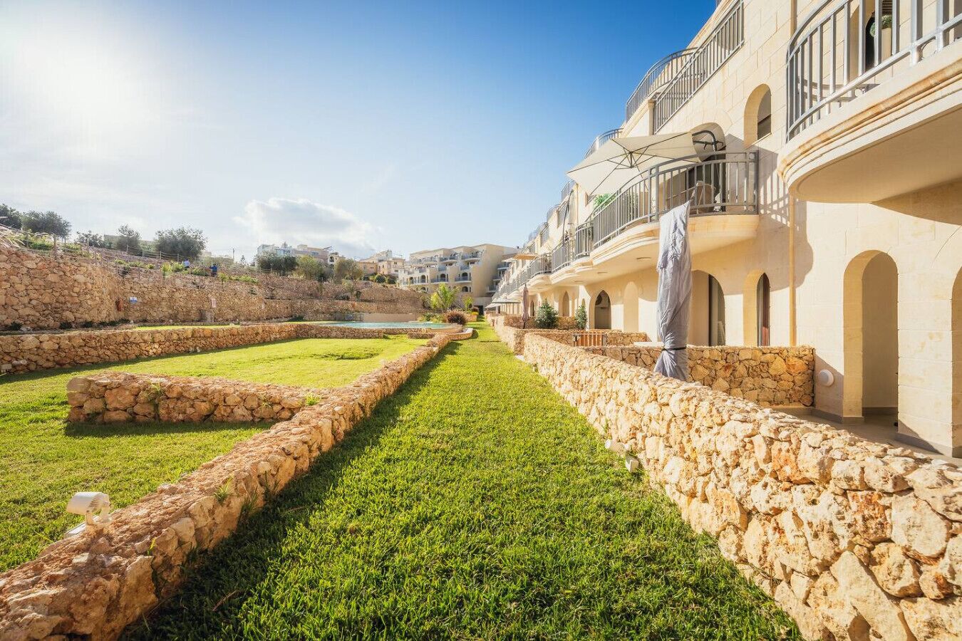 A courtyard with stone walls, a grassy lawn, and a building with balconies and arched windows.