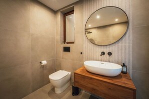 A modern bathroom with a large round mirror, a white toilet, and a wooden vanity with a sink. - Qala Skyview Penthouse Pool Sunsets BBQ Area (Qala)