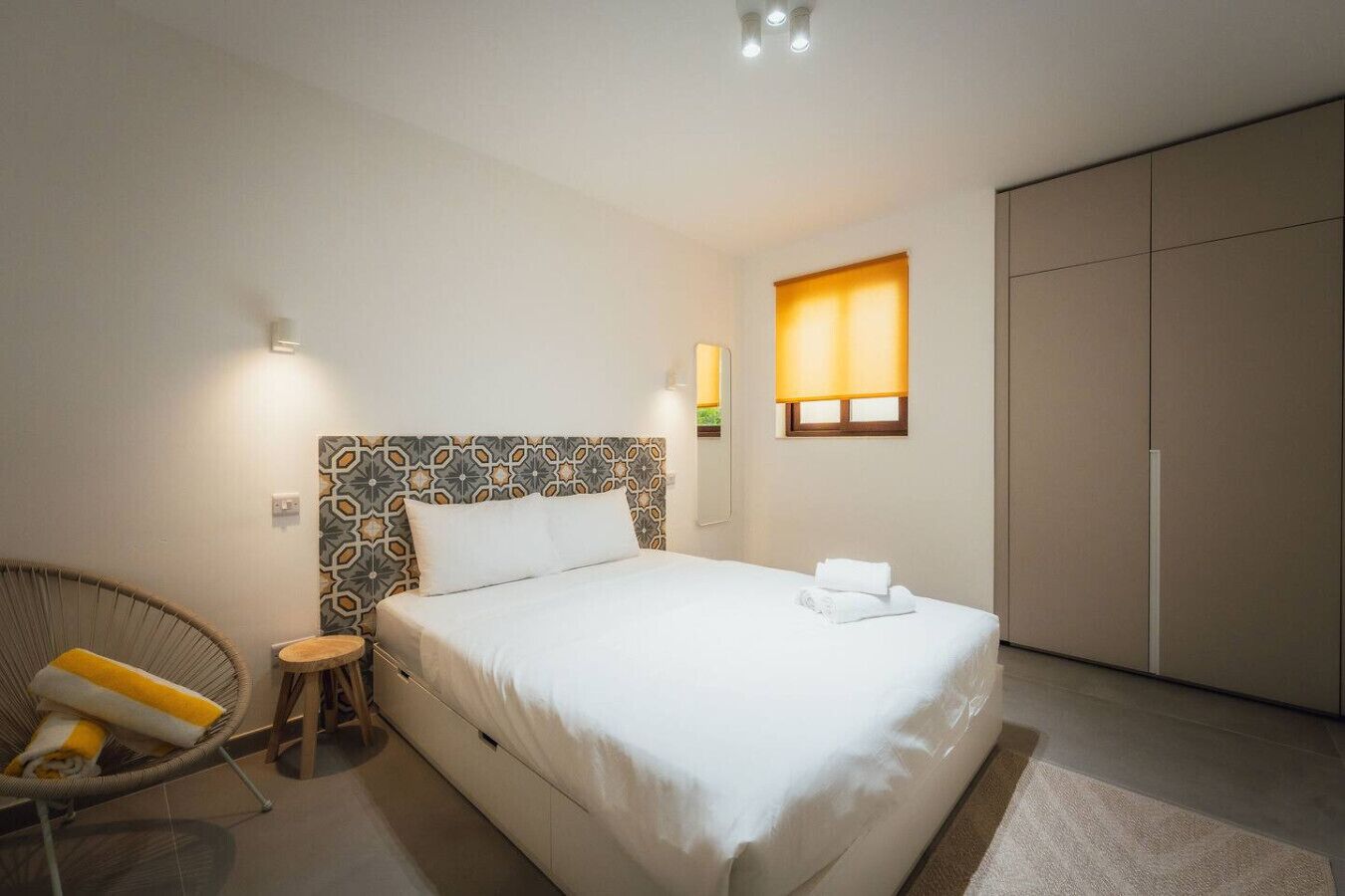 A bedroom with a bed, a chair, a wardrobe, and a window with a lamp.